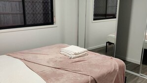 Ein Schlafzimmer mit einem Bett, einem Fenster, einem Spiegel und einem Nachttisch.