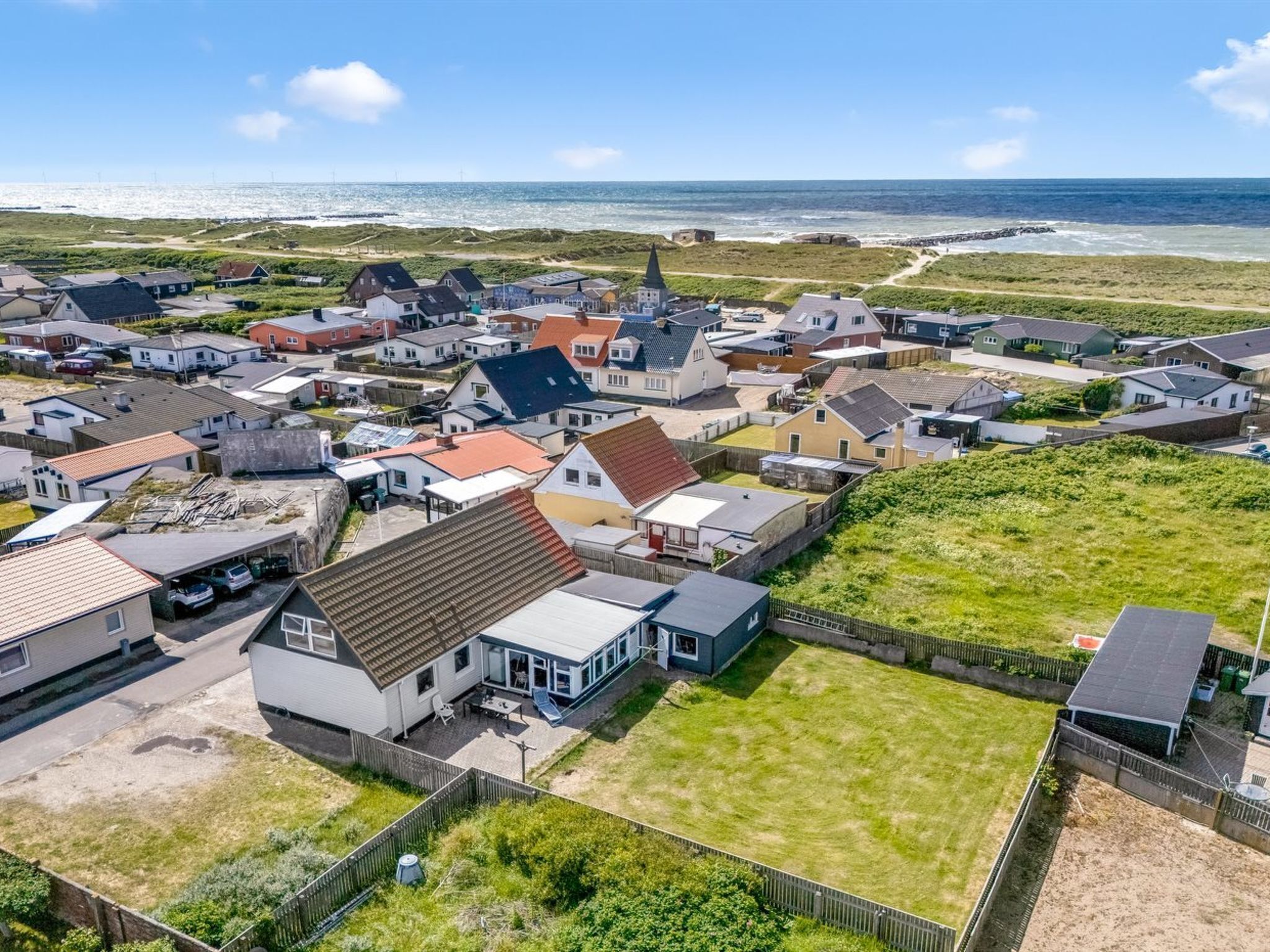 An aerial view of a coastal residential area with houses, a church, and a beach in the background.