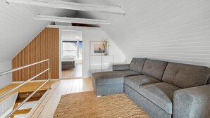Un dormitori tipus loft modern amb un sofà seccional gràveu gran, una escala de fusta i vista a la ciutat.