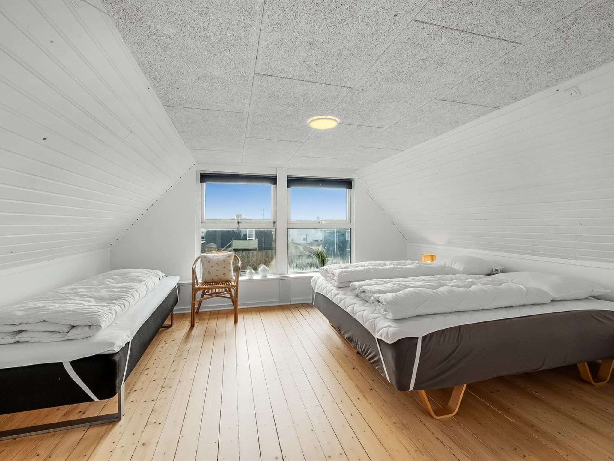 A bedroom with two beds, a chair, and a large window with a city view.