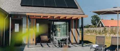 A modern house with a solar panel roof, a covered patio with outdoor furniture, and a clear view of the surrounding area.