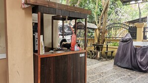 A wooden reception desk with a sign labeled "RECEPTION" in a courtyard with stone flooring, surrounded by greenery and a metal gate.