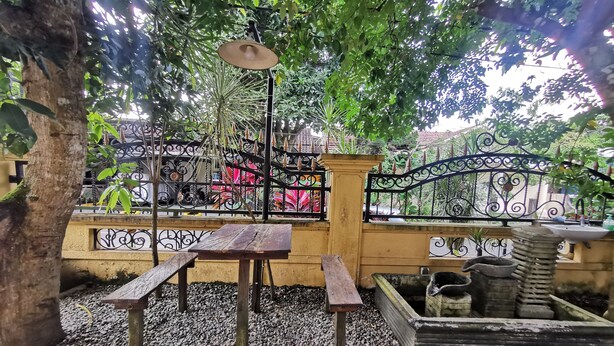 An outdoor seating area with wooden benches and a table, surrounded by a decorative metal fence and potted plants.
