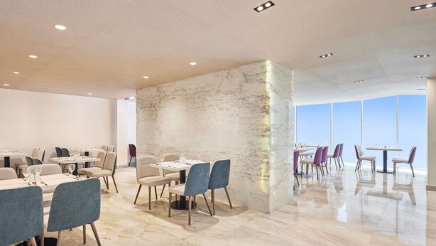 A modern dining area with marble walls and a high ceiling. Tables are set with chairs, and the floor is polished. - Nur Al Naseem  (Makkah)