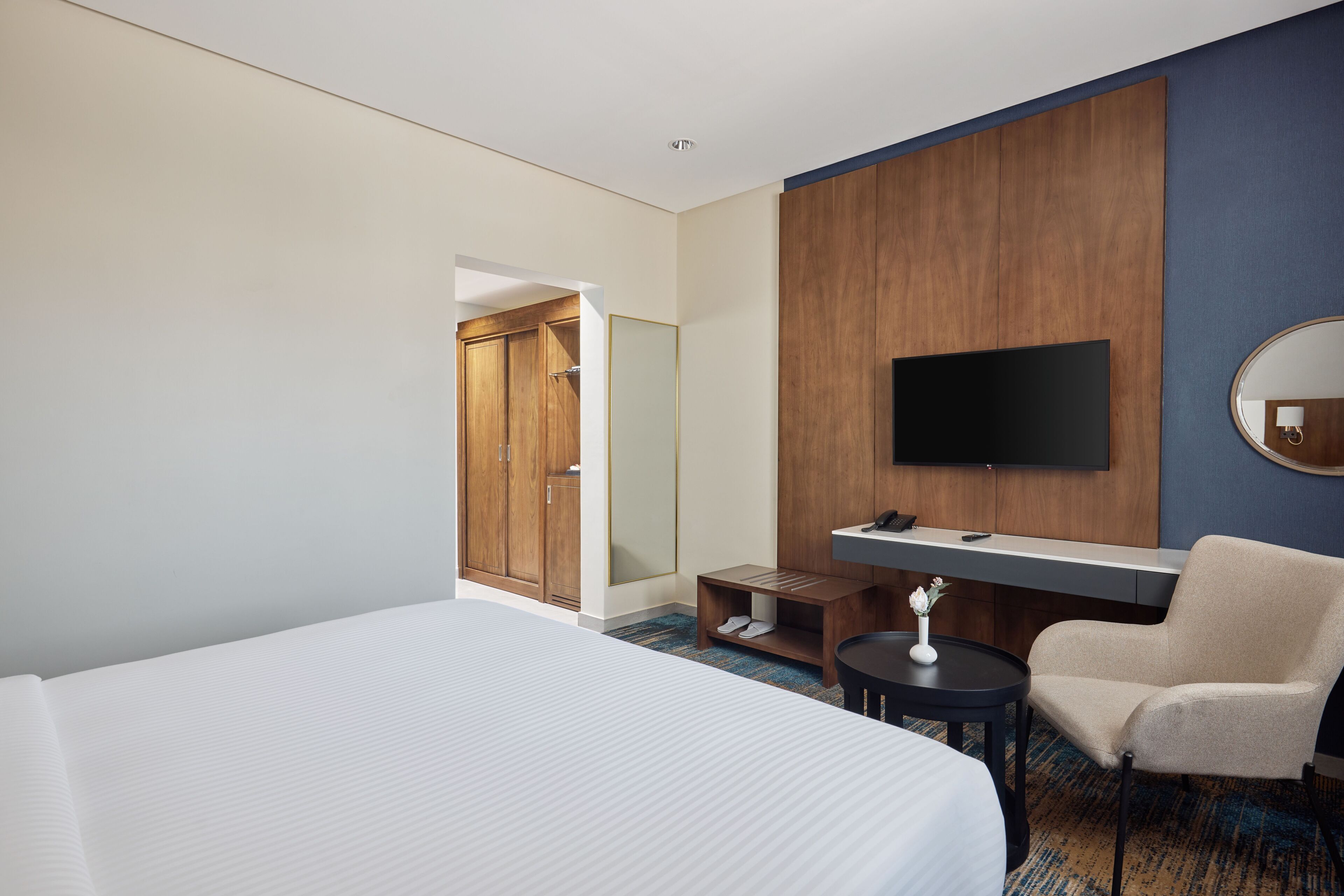 Quarto de hotel com uma cama grande, uma escrivaninha com cadeira, uma televisão e um guarda-roupa.