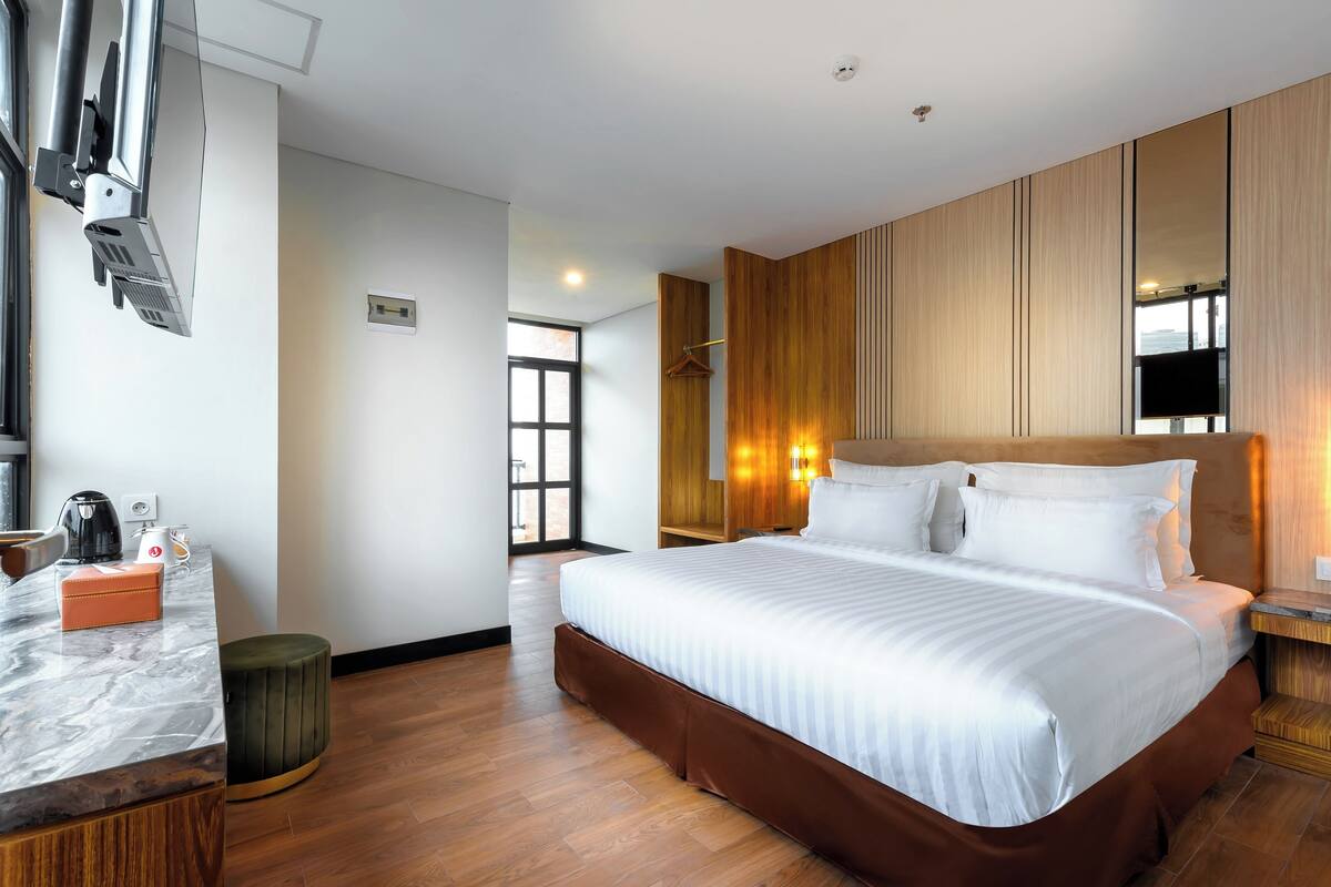 Ein modernes Hotelzimmer mit einem großen Bett, einer Wandpaneele aus Holz, einer Marmorplatte und einem Fernseher.