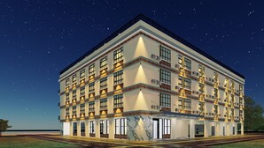 Een meerlaags hotel met een modern ontwerp, herkenbaar aan een opvallende ingang met een marmeren gevel, meerdere balkons en een reeks airconditioners.