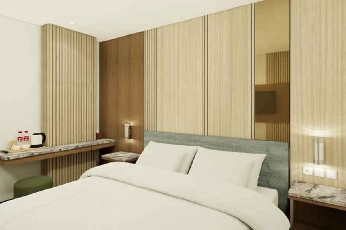 Una habitación de hotel con cama, mesitas de noche y televisor montado en la pared.