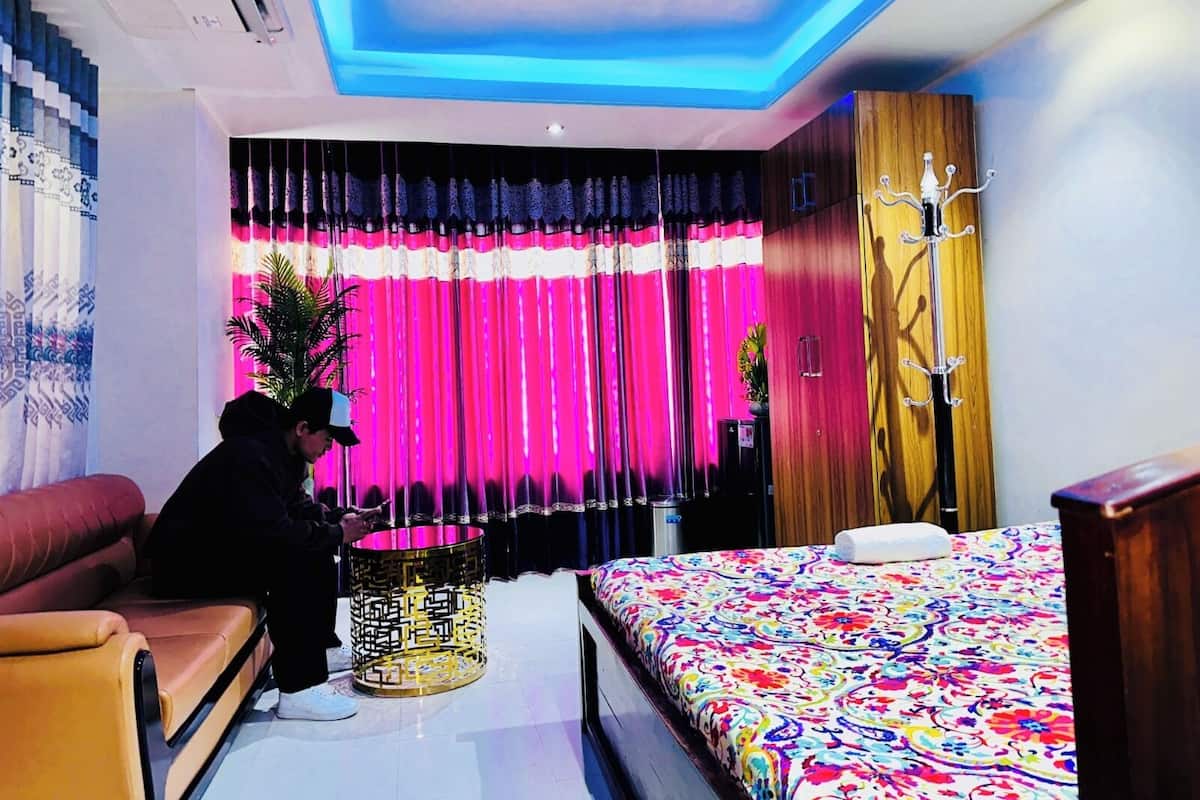 Quarto de hotel moderno com cama, sofá, abajur decorativo e cortinas.