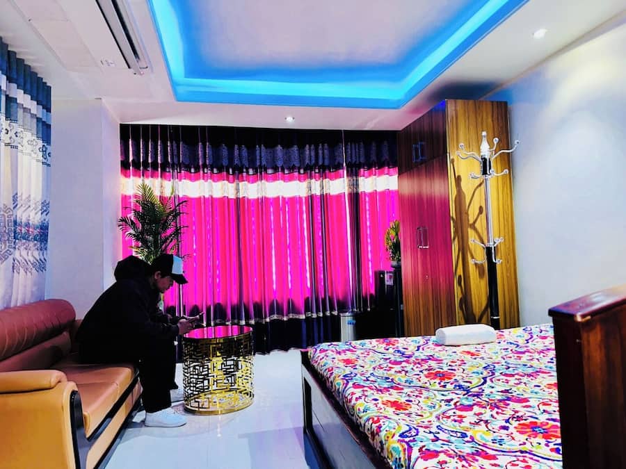 A modern hotel room with a bed, a sofa, a decorative lamp, and curtains.