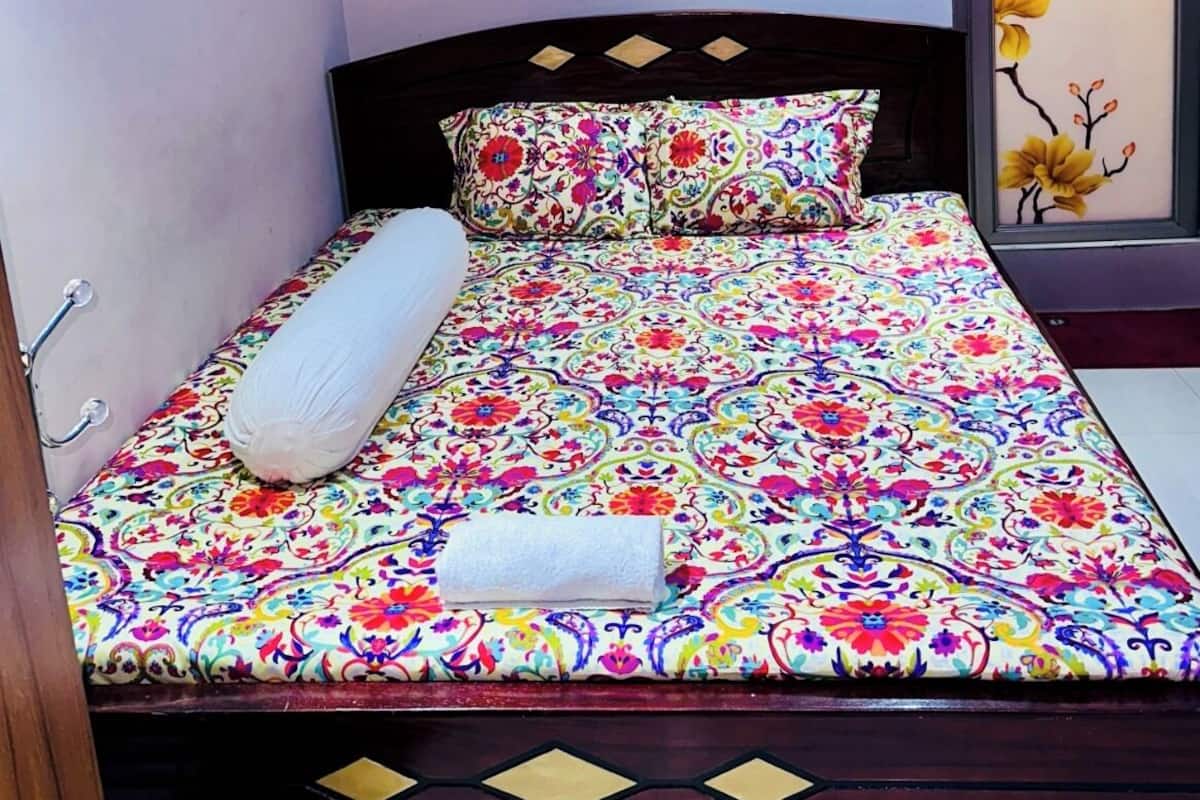 Uma cama com colcha florida, um travesseiro branco e outro a combinar em uma cabeceira de madeira.