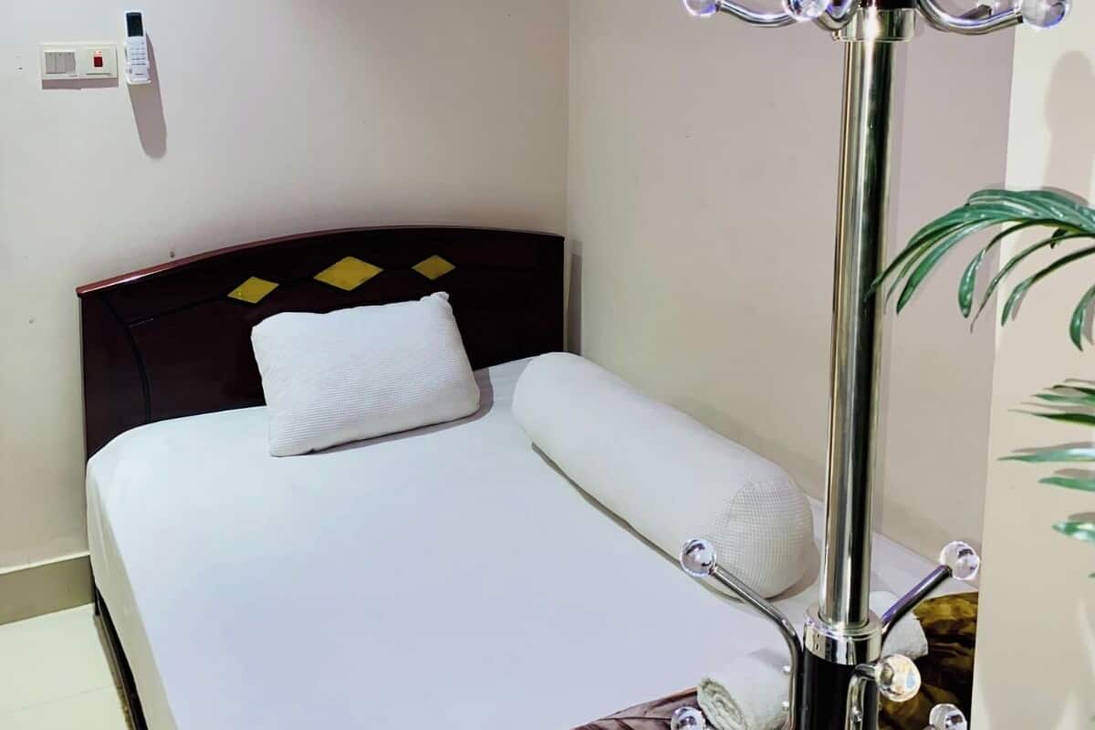 Quarto de hotel com cama bem arrumada, mesa de cabeceira com abajur e tomada na parede.