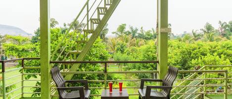Un área de estar al aire libre con techo, con dos mesas y sillas, con vista a un exuberante jardín y una escalera.