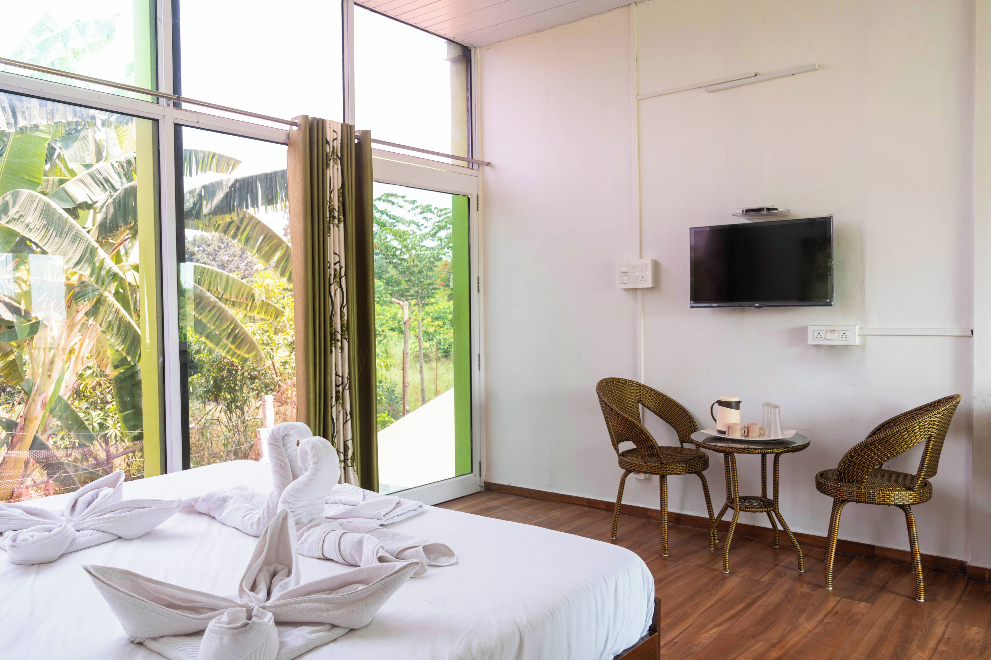 Habitación de hotel con cama, televisor, sillas de mimbre y vistas a zonas verdes.