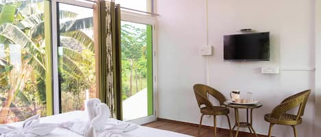 Habitación de hotel con cama, televisor, sillas de mimbre y vistas a zonas verdes.