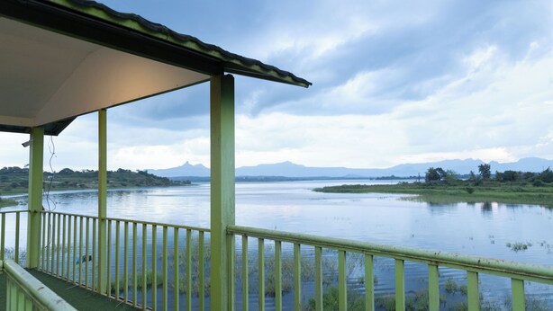 A covered outdoor area with a view of a calm lake and distant mountains. - The Riverine Stays by Igatpuri (Igatpuri)