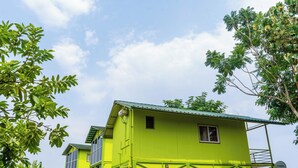 A bright green two-story building with a satellite dish, surrounded by lush greenery. - The Riverine Stays by Igatpuri (Igatpuri)