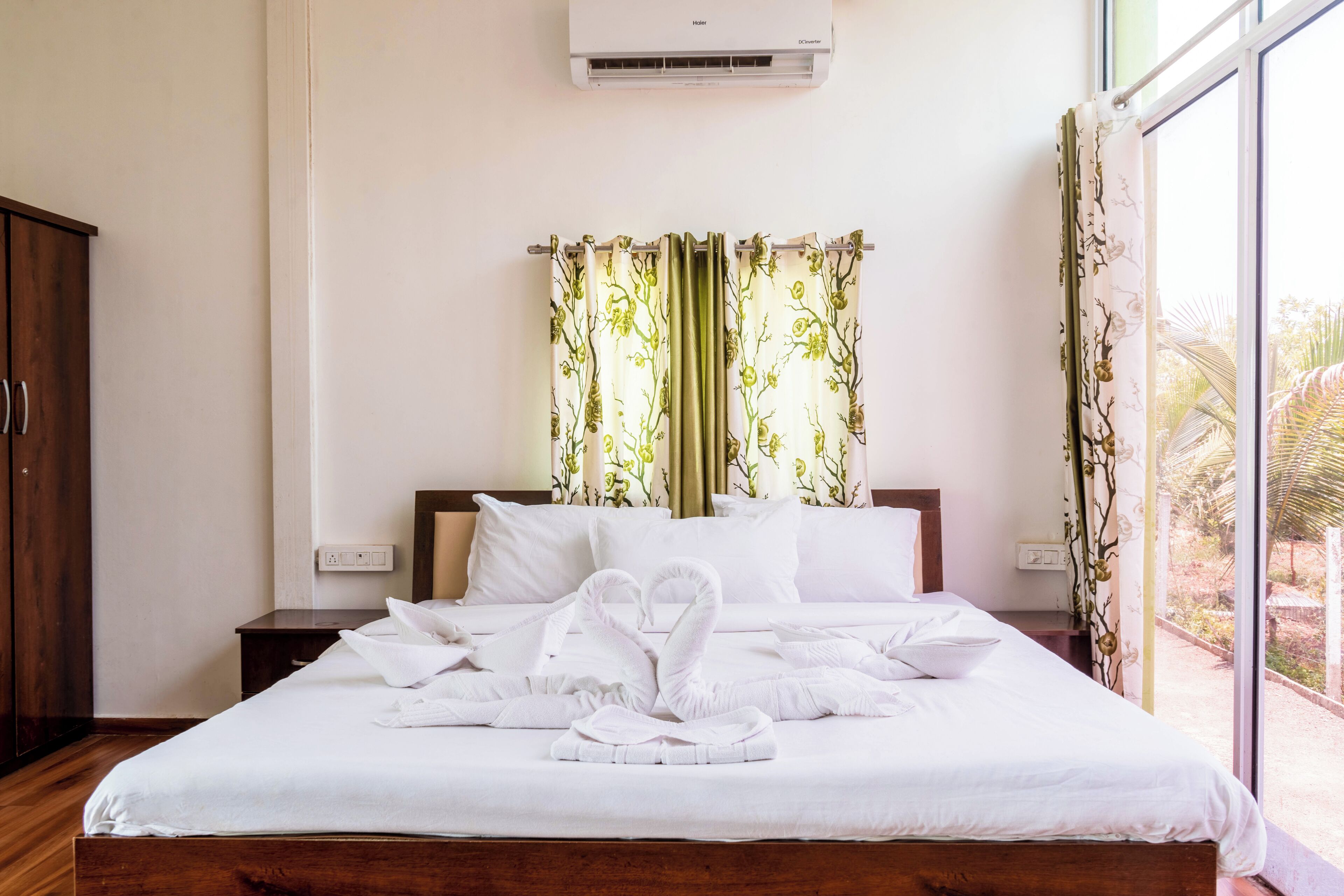 A hotel room with a neatly made bed, a wooden wardrobe, and a window with curtains.