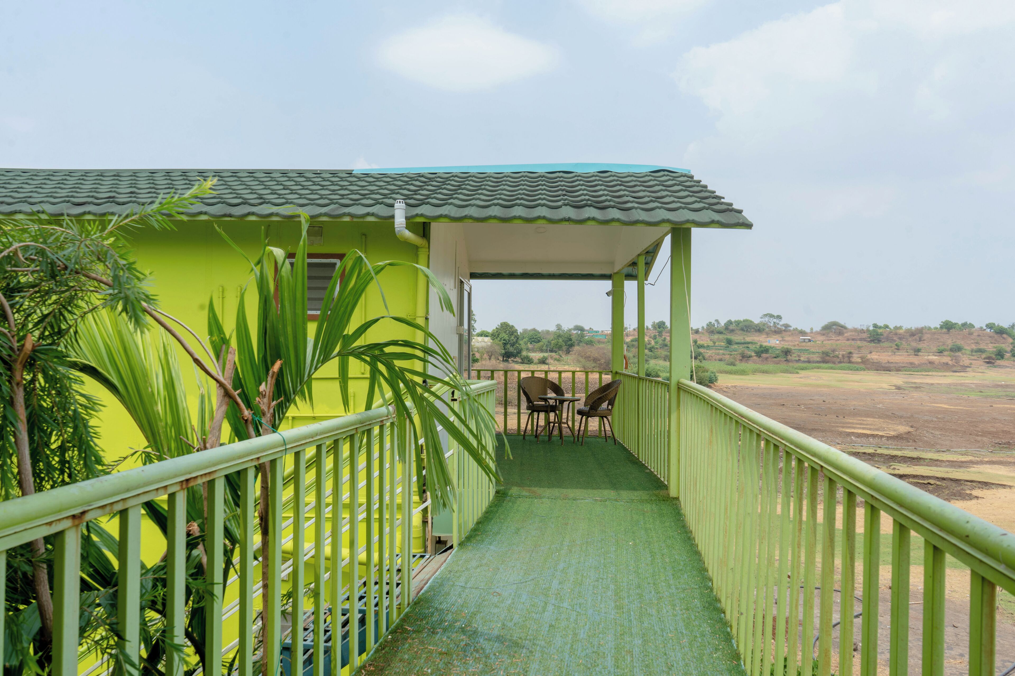 A green building with a covered porch, a small table, and chairs.