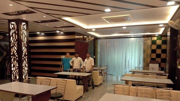 A modern dining area with multiple tables and chairs, a decorative wall with a checkered pattern, and a ceiling with recessed lighting. - Hotel Mayur Palace (Agra)