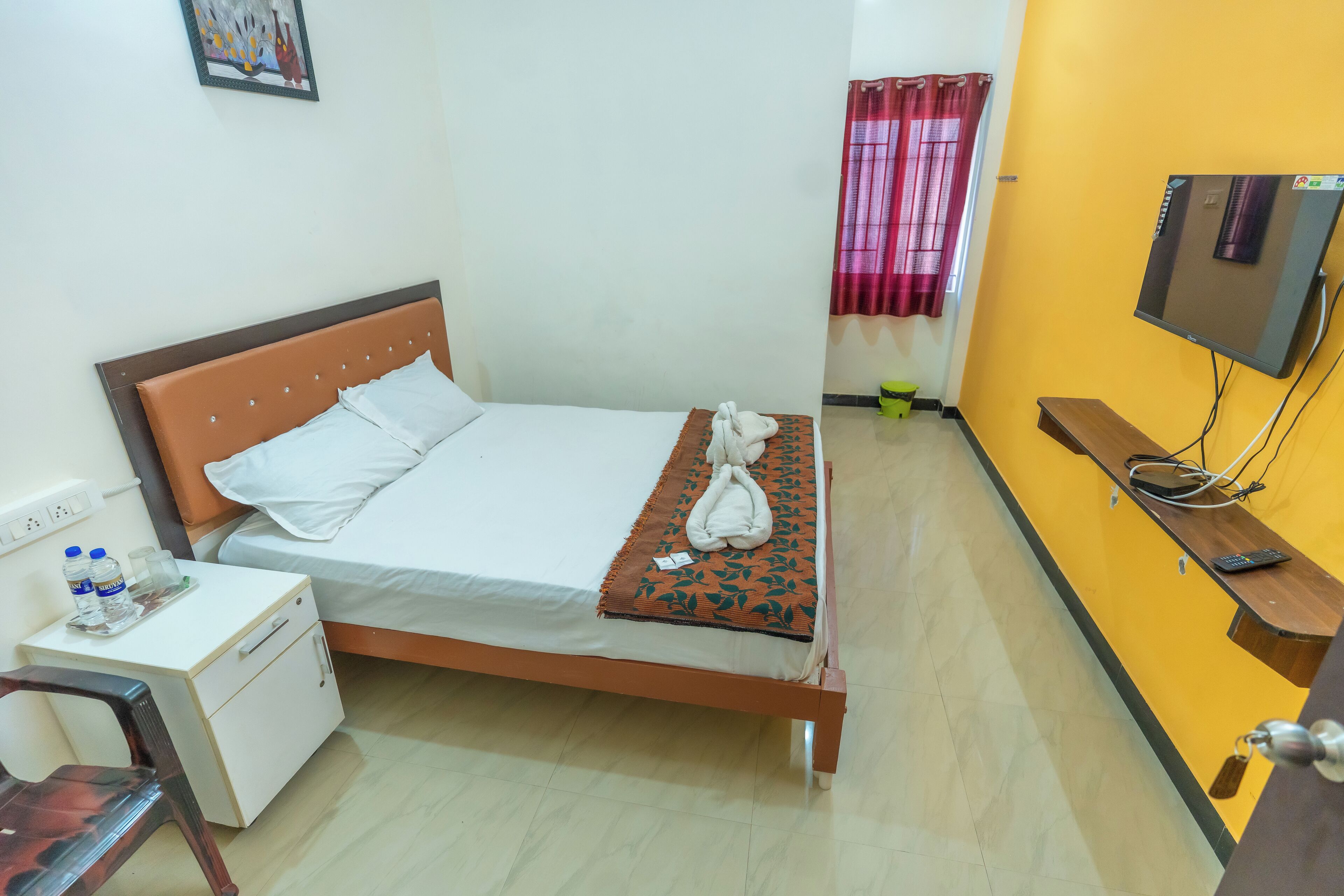 A single bed with a wooden headboard, a bedside table with a water bottle, and a TV mounted on the wall.