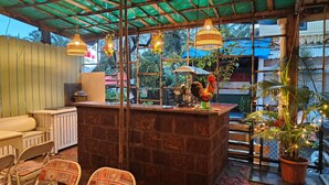 A cozy outdoor seating area with a brick counter, wicker hanging lights, and a decorative rooster statue. - Hotel Baga Stays By Coral (Calangute)