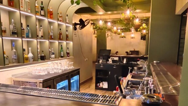 A bar area with a counter, shelves of bottles, and hanging plants. - Hotel Baga Stays By Coral (Calangute)