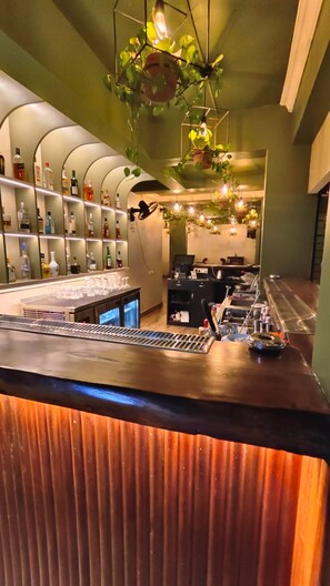 A bar area with a counter, shelves of bottles, and hanging plants. - Hotel Baga Stays By Coral (Calangute)