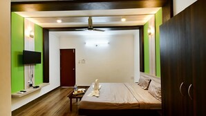 A hotel room with a bed, a flat-screen TV, a ceiling fan, and a wooden floor. - Hotel Baga Stays By Coral (Calangute)