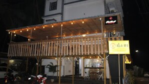 A building with a covered outdoor seating area, a sign with a logo, and a parked motorcycle. - Hotel Baga Stays By Coral (Calangute)