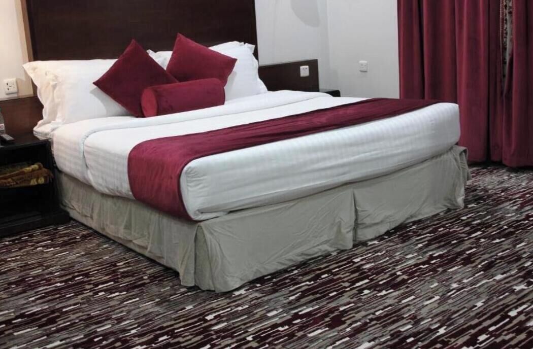 A hotel room with a bed, a nightstand, a lamp, and a patterned carpet.