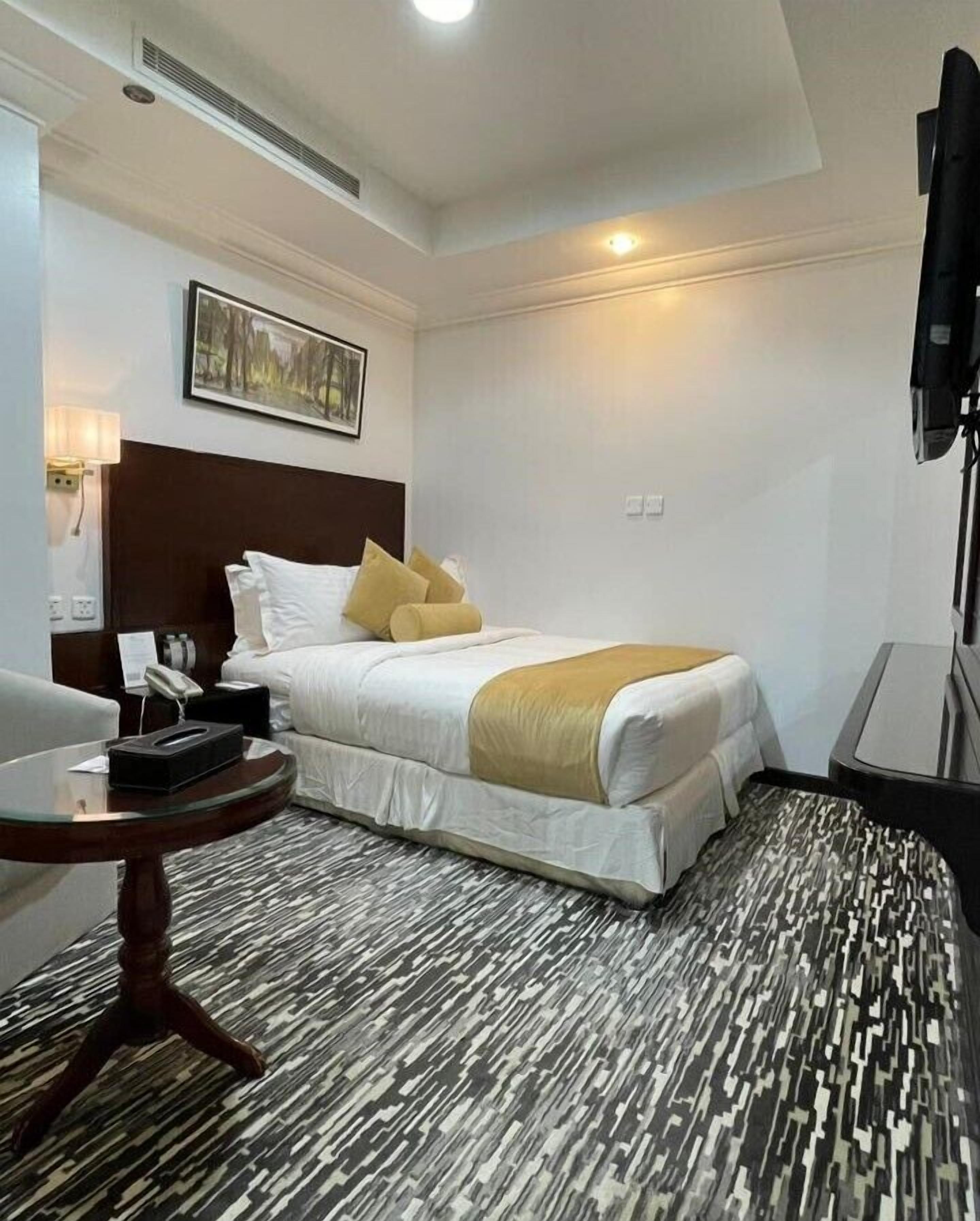 Une chambre d’hôtel avec un lit, un bureau, une chaise, une télévision et un tableau au mur.