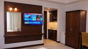 Habitación de hotel con televisión montada en la pared, cama, armario y una pequeña kitchenette.