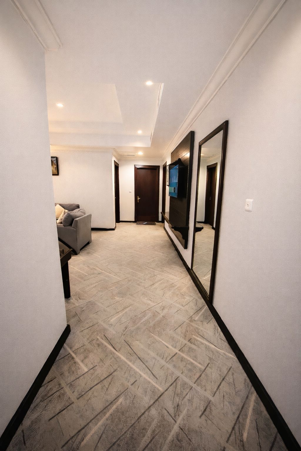 A hallway with a patterned carpet, a sofa, a door, and a large mirror.