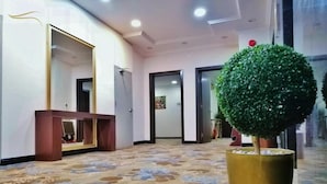Un vestíbulo de hotel con alfombra estampada, un árbol grande en maceta y un espejo en la pared.