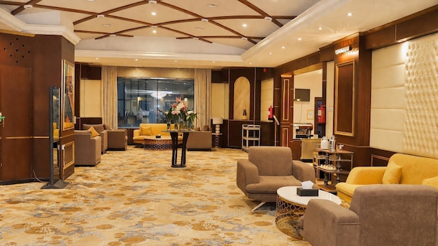 Un hall de hotel con alfombra estampada, sofás, una mesa de centro y un ventanal grande.