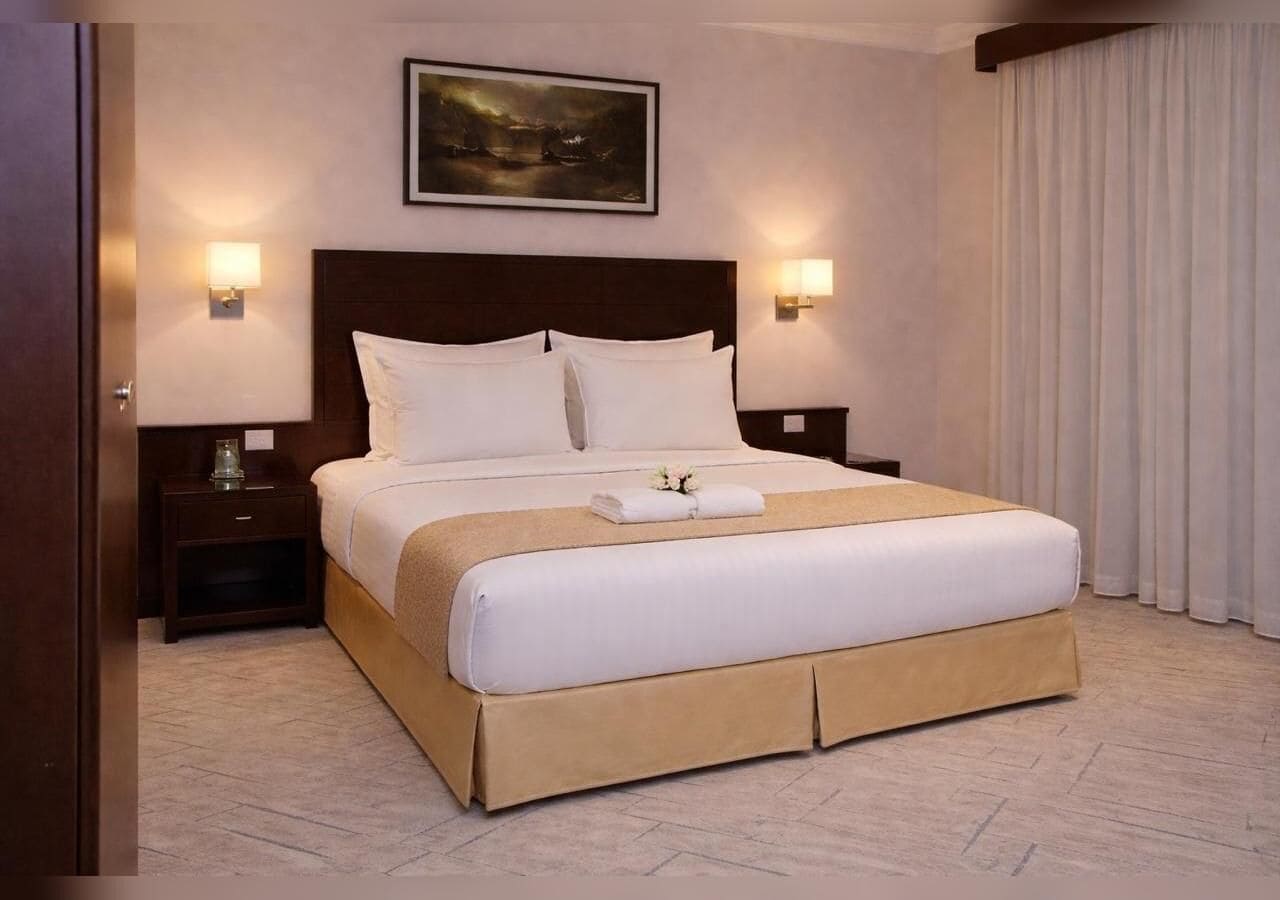 A hotel room with a large bed, two bedside tables, a painting on the wall, and a window with curtains.