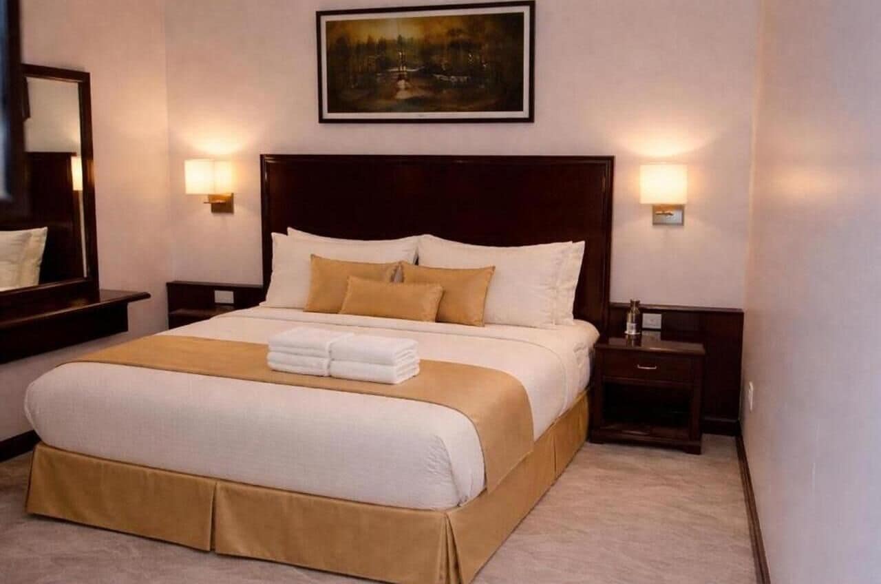 Habitación de hotel con una cama grande, dos mesitas de noche, un tocador, un cuadro en la pared y un espejo.