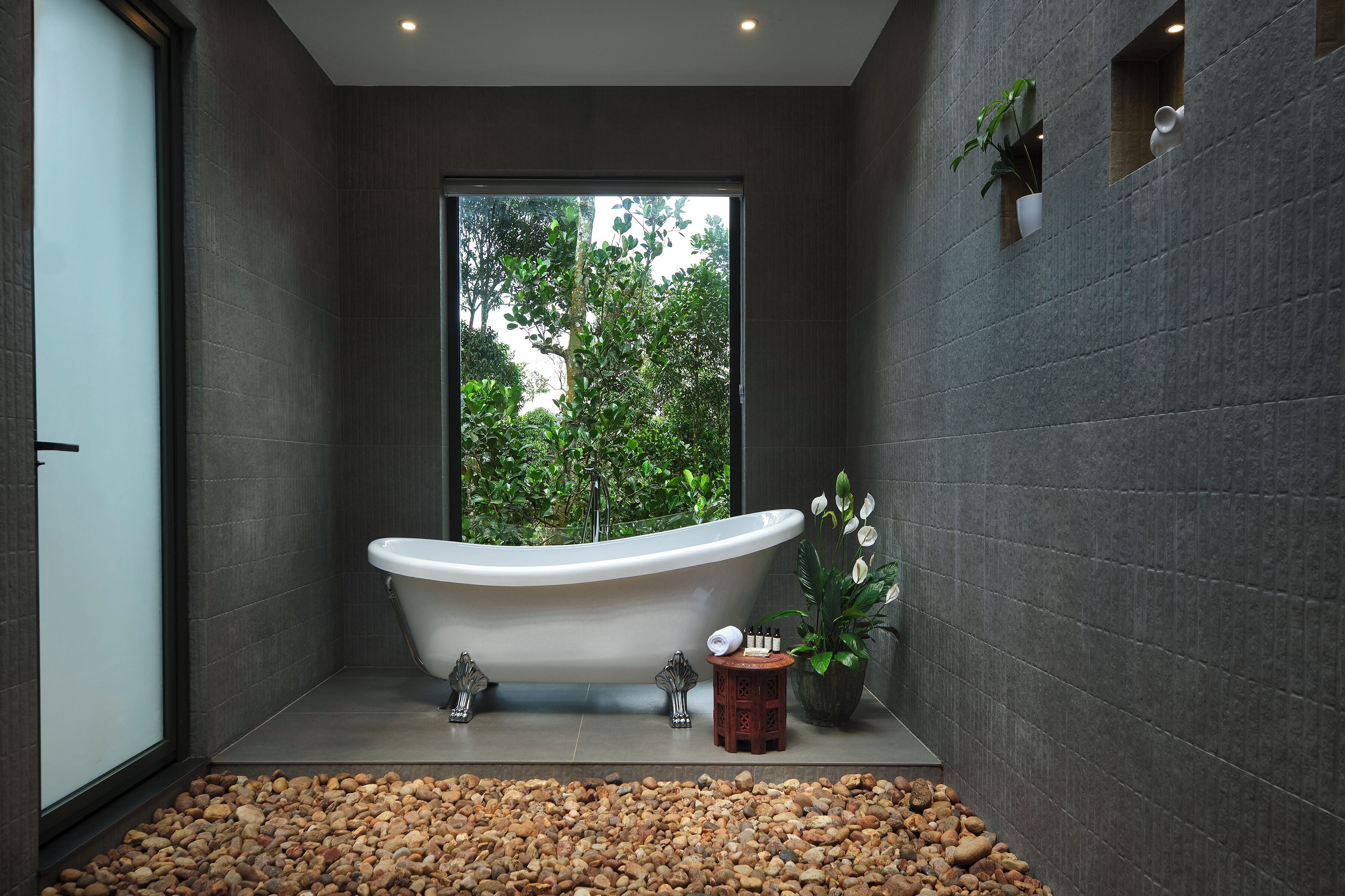 A modern bathroom with a freestanding bathtub, a small wooden stool, and a potted plant.