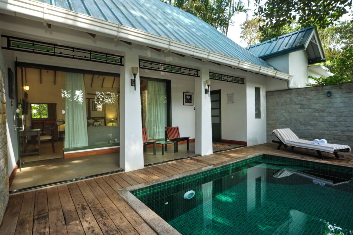 A poolside area with a wooden deck, a lounge chair, and a glass-enclosed patio with a dining table and chairs.