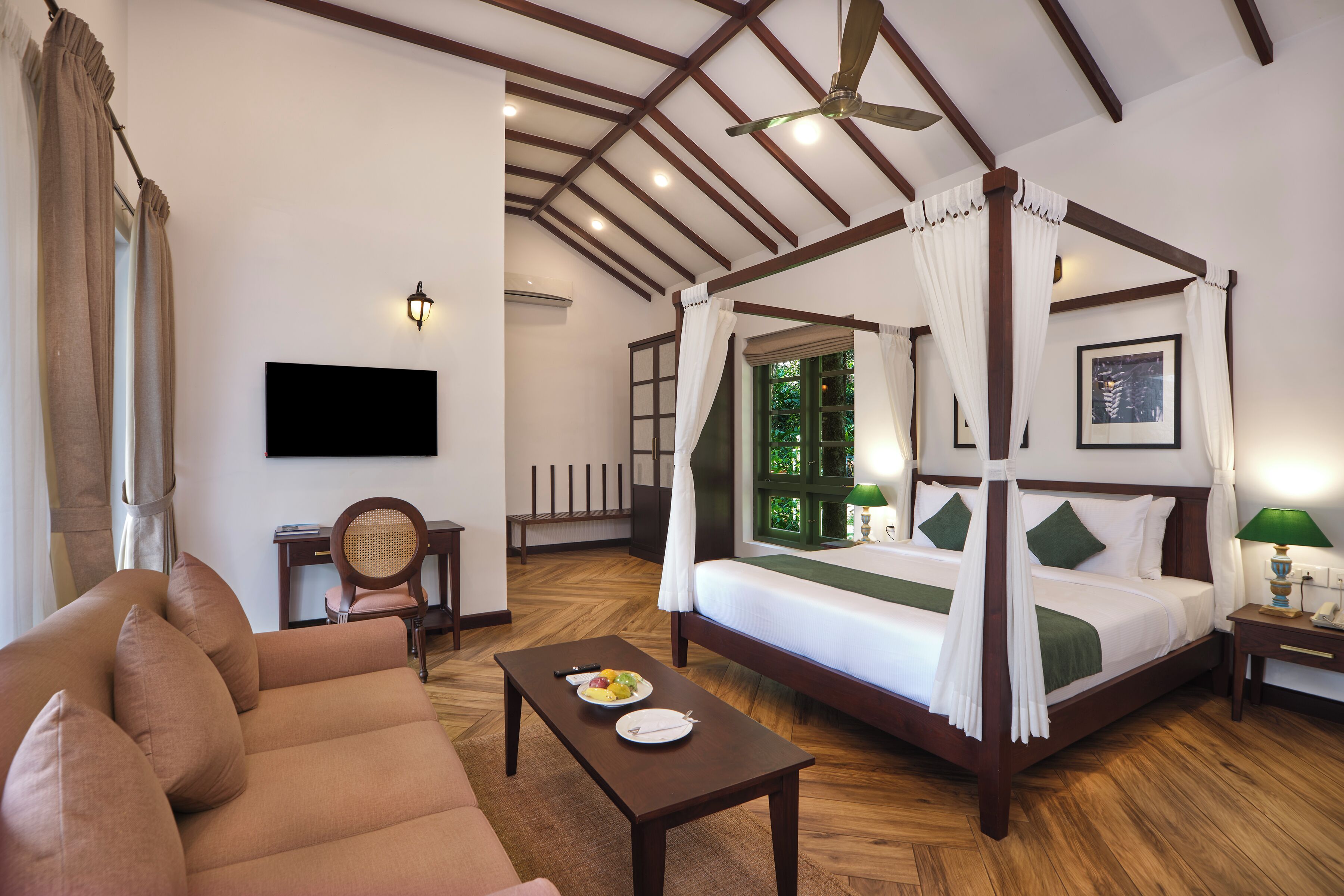 A well-lit room with a four-poster bed, a sofa, a dining table with plates, and a television on the wall.