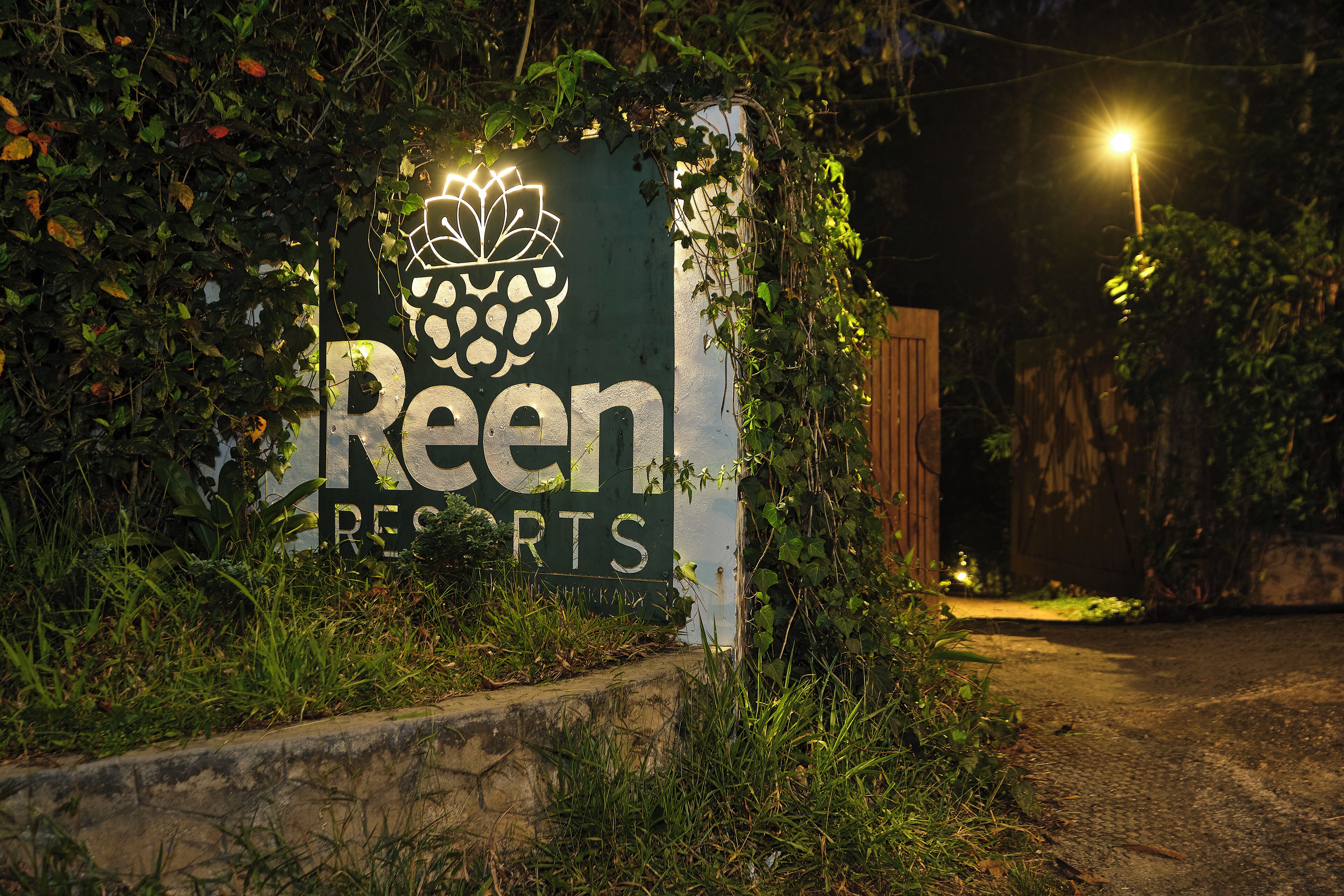 Señal de 'Reen Resorts' con logotipo de flor de loto, rodeada de follaje.