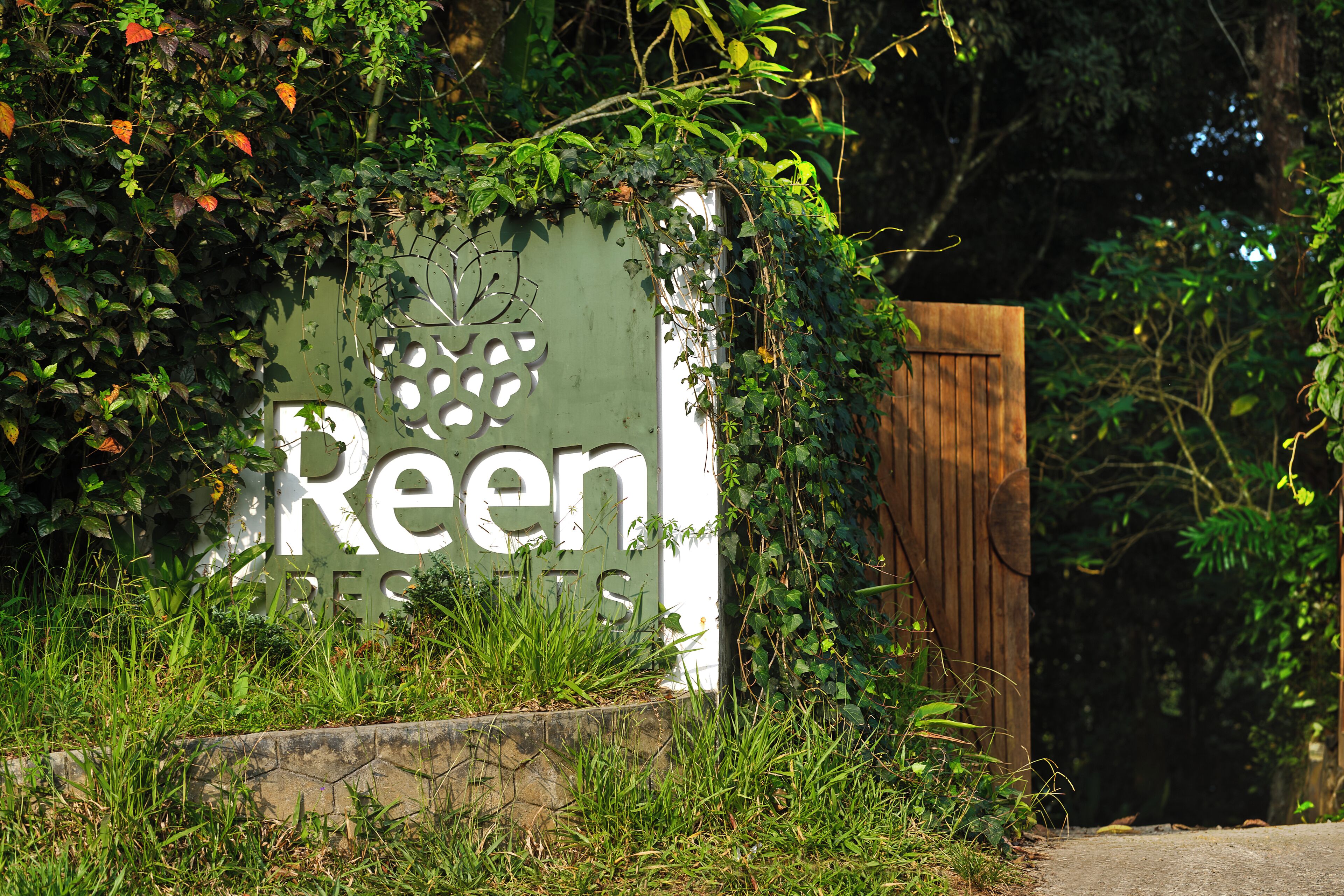 A sign for 'Reen Residences' partially covered by greenery.