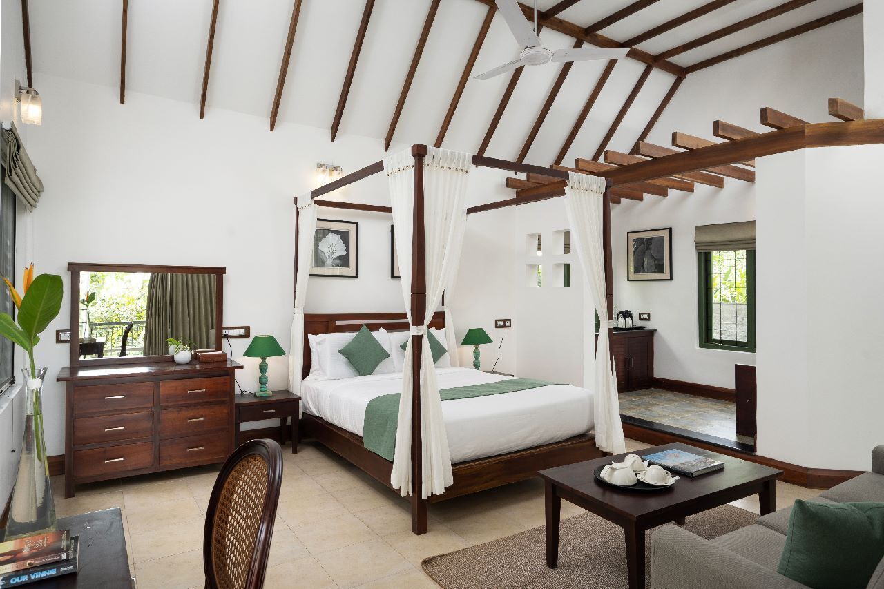 A four-poster bed with a canopy, a wooden dresser, a desk with a chair, and a small table with a book and teapot.