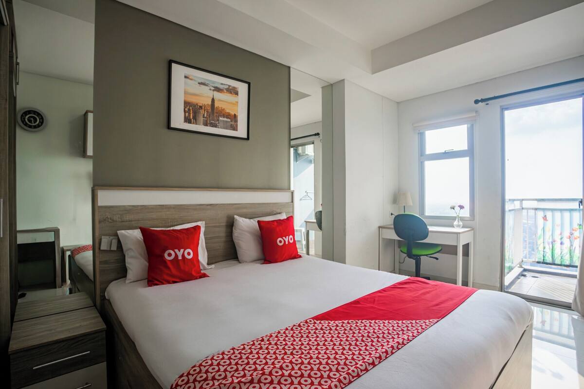 Ein Hotelzimmer mit einem großen Bett, einem Schreibtisch mit Stuhl, einem kleinen Tisch mit Lampe und einem Balkon mit Blick.