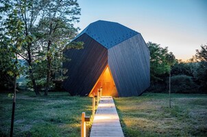 Um edifício moderno e geométrico com um design angular peculiar, cercado por uma área gramada e árvores.