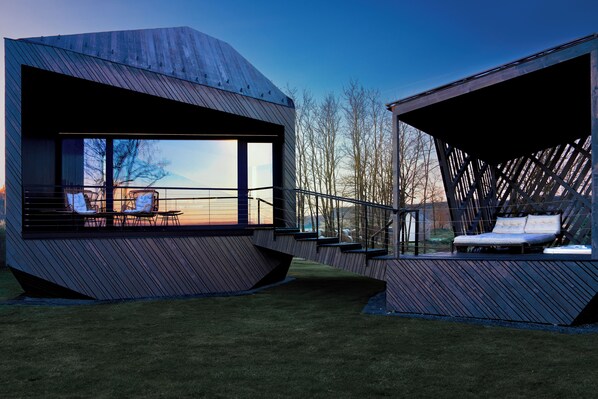 A modern house with large windows, a balcony, and a lounge area with chairs. - Rock Cabins (Vigántpetend)