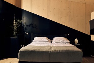 Quarto moderno com cama, mesas de cabeceira e apoio para objetos pessoais.