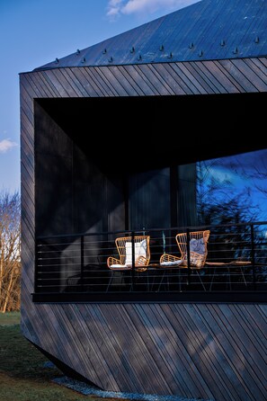 A modern building with a unique angular design and a large windowed balcony with wicker chairs. - Rock Cabins (Vigántpetend)
