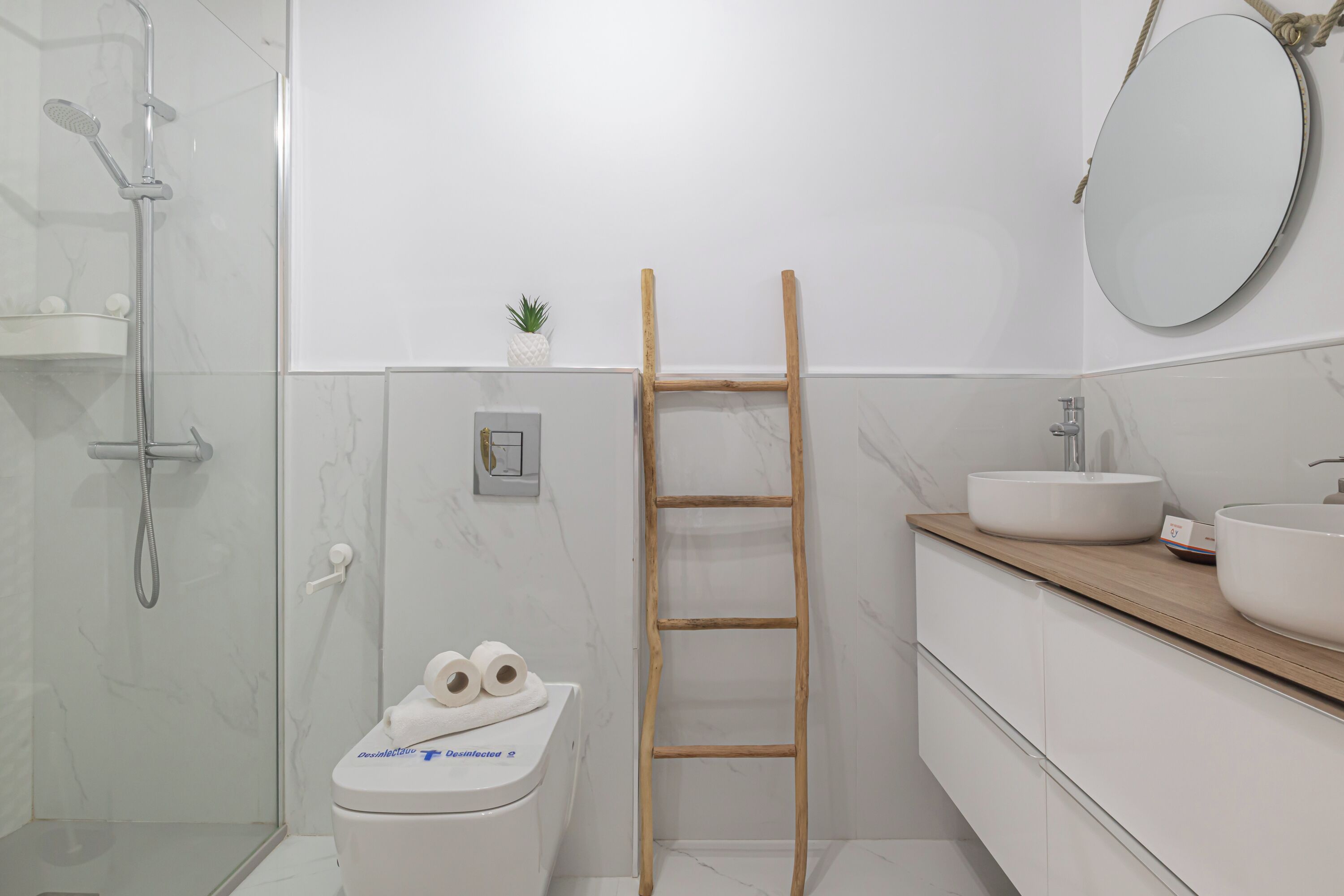 Un baño con inodoro, ducha, escalera de madera, lavabo y espejo.